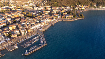 Fototapeta premium Aerial view with drone of the city of Garda. Town on the lake of the same name, blue sea at sunset, seagulls and boats in the distance.