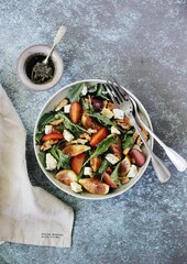 Salad with figs, tomatoes, nuts, cheese, greens, plums and sprinkled with honey