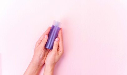Hands hold cosmetic blue bottle on blur pink background with copy space