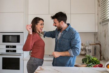 Young couple goofing around and dancing in their kitchen.