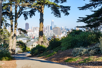 View of San Francisco downtown skyline from a winding paved path in a hilltop public park on a sunny autumn day
