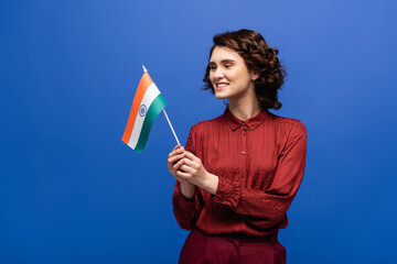 cheerful language teacher holding flag of India and looking at camera isolated on blue.