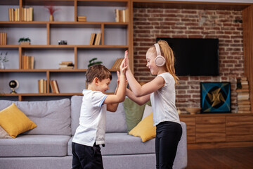 Children jump and dance at home while listening to music on headphones. Having fun. Family concept.