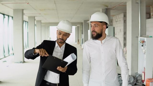 Indian and arabian builders engineers workers in helmets walking on construction at sunlight survey urban meeting skyscraper