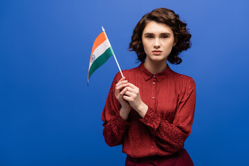 curly language teacher holding flag of India and looking at camera isolated on blue.