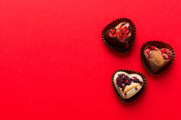 chocolate sweets in the form of a heart with fruits and nuts on a colored background. top view with space for text, holiday concept