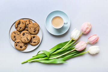 Cup of coffee mug with coffee, cookies and tulips on a colored background. Greeting spring card top view