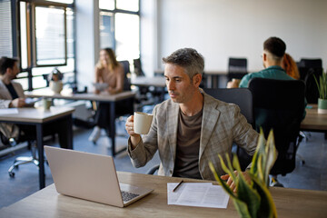 
Shot of a mature businessman using a laptop and having coffee in a modern office