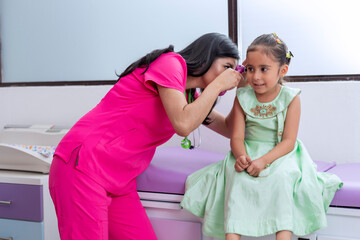 Pediatrician doctor checking the ear of a little girl in her medical office