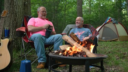 Obraz premium Two gay men sitting with each other, talking and smiling while sitting in front of a campfire in a forest.