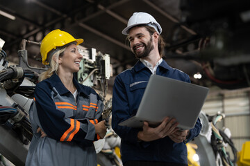 Happy male and female engineers with laptop checking and maintaining robot arm welding machine at assembly robotic factory industry