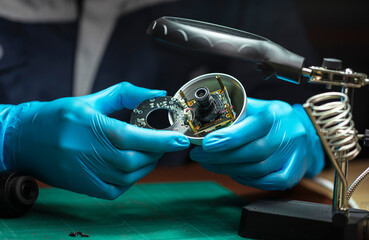 Close-up of a male technician wearing gloves checking the circuit board of cctv camera in workshop