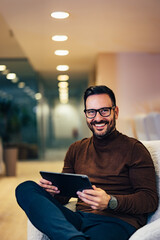Portrait of a smiling businessman holding a tablet, sitting at the office.