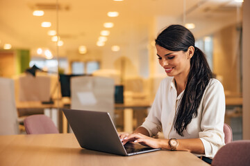 Smiling female boss using a laptop, working on a new project, sitting at the office.