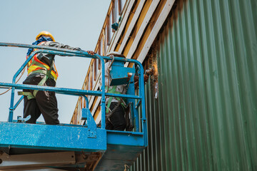 Two workers man on Scissor hydraulic lift or X-lift and use Electric wheel grinding or angle grinder on factory roof at a construction site, Mobile aerial work platform
