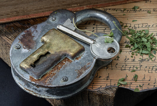 The Key and the Vintage Iron Padlock with chopped cannabis leaves on the old vintage music note with the old wooden plank background.
