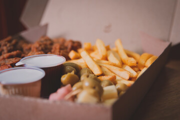 French fries in a box with assorted snacks on a wooden table.