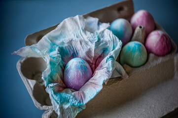 Colorful easter eggs in carton box  on table. Handmade painted egg in paper napkin. Soft focus.