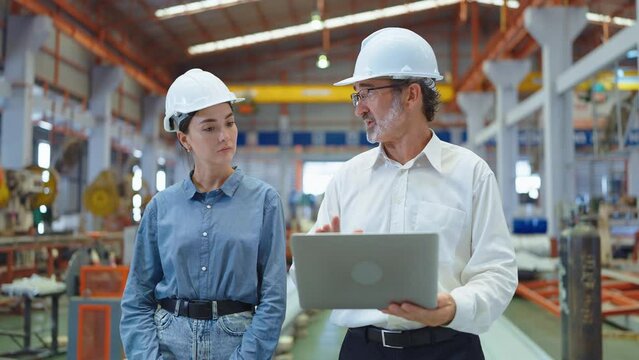 Two professional engineer man and woman manager leader wearing helmet and holding laptop walking in factory talking and discussing for work