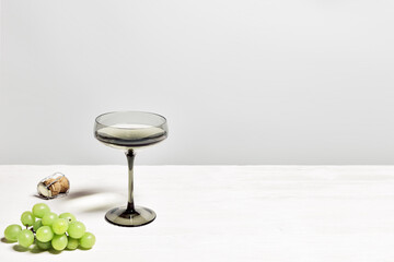 Gray shampagne glasses and grape om white wooden table, trend wine glass colored. Minimal summer still life with sparkling white wine in wide shampagne glass. Side view, copy space