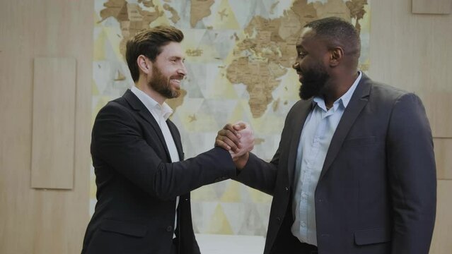 Two multiethnic big businessmen shaking hands in the office against the backdrop of the world map. Successful transaction of large transcontinental corporations. African and European businessmen.
