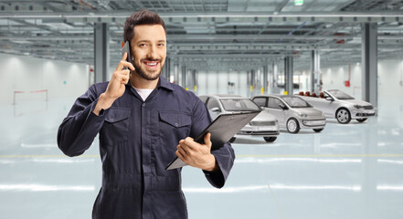 Worker in a blue uniform using a mobile phone and holding a clipboard inside a garage