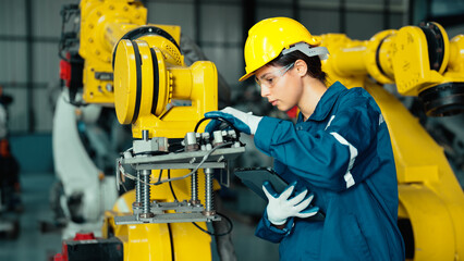 Caucasian mechatronics engineer is inspecting a lot of robotic arms in warehouse before being used in factory. A female industrial worker is using a tablet to record the results of examining machines.