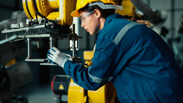 Caucasian mechatronics engineer is inspecting a lot of robotic arms in warehouse before being used in factory. A female industrial worker is using a tablet to record the results of examining machines.