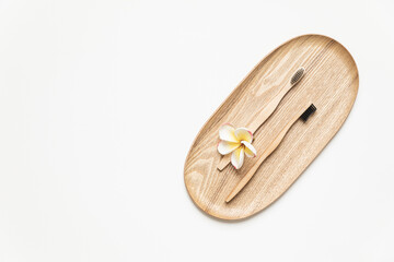 Bamboo toothbrush on a table with copy space on a white background. Styled composition of flat lay with tropical flowers.