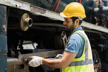 Male engineer worker maintenance locomotive engine, wearing safety uniform, helmet and gloves in locomotive garage. Male railway engineer repair railhead engine in garage