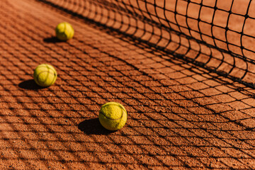 Light orange empty outdoor clay court surface dry grungy ground baseline detail for playing tennis with net shadow in sunny day, yellow green balls, gravel texture background, copy space for text 
 - obrazy, fototapety, plakaty