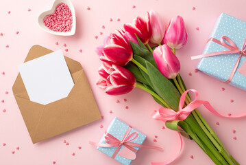 Mother's Day concept. Top view photo of bouquet of tulips blue gift boxes craft paper envelope with letter and heart shaped saucer with sprinkles on isolated pastel pink background with copyspace