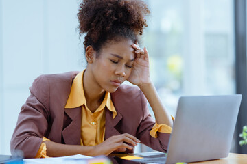 Young African American businesswoman working on laptop with documents and stressed over worked from...