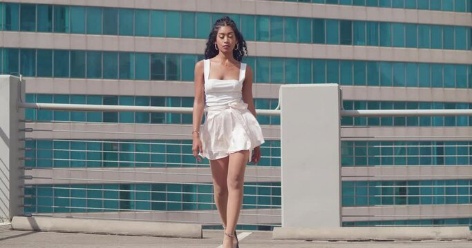 Pretty young latina walking on a rooftop in a mini skirt with tall buildings in the background