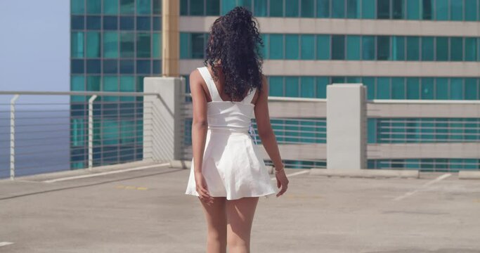 Young latina walking while her mini skirt blows in the wind on a rooftop car park in the city