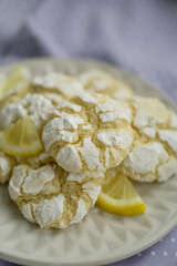 Delicious citrusy lemony snack, crunchy cracked lemon crinkle cookies coated with powdered sugar on white plate close up selective focus 