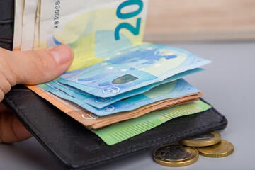 The hand holds euro banknotes and coins in the black wallet, close-up