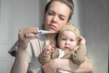 Mom measures body temperature baby by electronic thermometer. Sick child with high temperature....