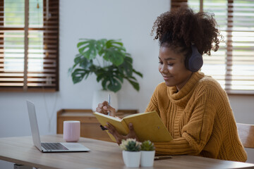 Young African woman holding a book with earphones sitting on sofa at home, young woman stay at home concept.