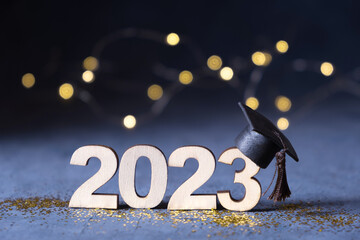 Class of 2023 concept. Wooden number 2023 with graduate hat on dark background with bokeh
