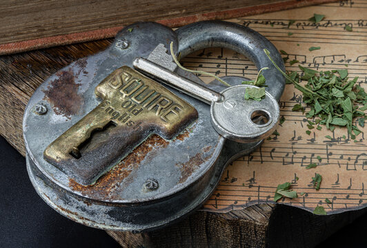 Bangkok,Thai - Mar 17, 2023 : The Key and the Vintage Iron Padlock with chopped cannabis leaves on the old vintage music note with the old wooden plank background.