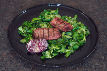 ready to eat - lamb's lettuce, red onions and roasted meat from a red deer calf on a black plate