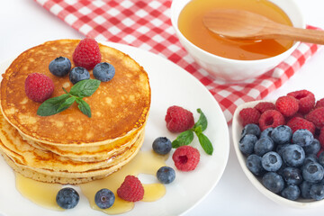 American pancakes with fresh blueberry, raspberry and honey served on white plate. Healthy morning breakfast.