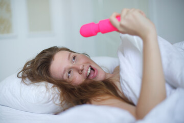 Young happy sexy woman hold in hand sex toy, masturbate with vibrator in bed in bedroom at home.