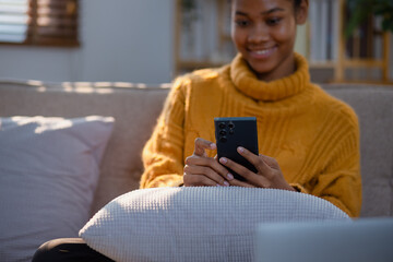 Young African American woman using smart phone at home. Happy beautiful black girl thinking while using mobile phone. social media.