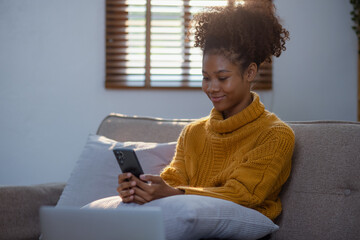 Young African American woman using smart phone at home. Happy beautiful black girl thinking while using mobile phone. social media.