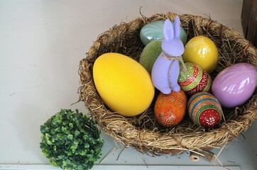 Osterdekoration mit bunten Eiern aus Holz mit Muster und blauem Hasen aus Filzstoff auf weißem...