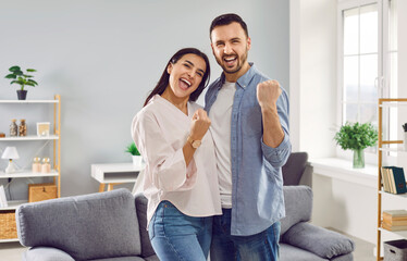 Portrait of a happy excited overjoyed couple family with yes gesture standing in the living room at...