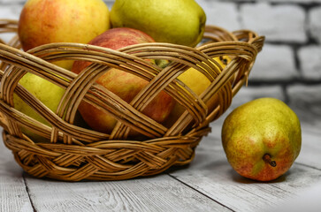 Pear and wicker basket with apples and pears on the background of a white brick wall.