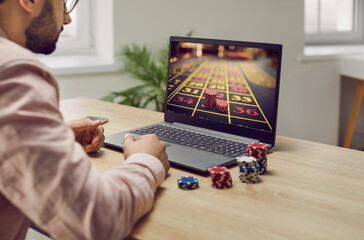 Young man with unshaven bristles sitting at the desk and playing gambling betting on the internet...